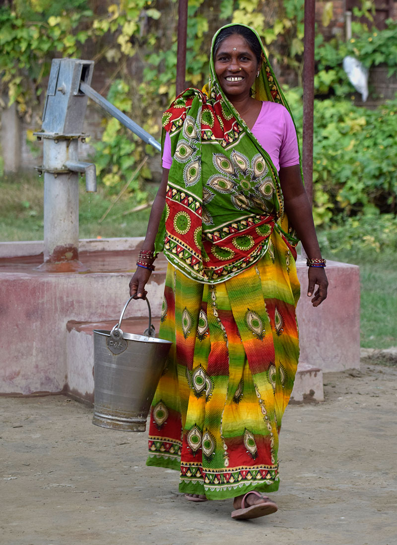 woman carring bucket of water with faucet in the background
