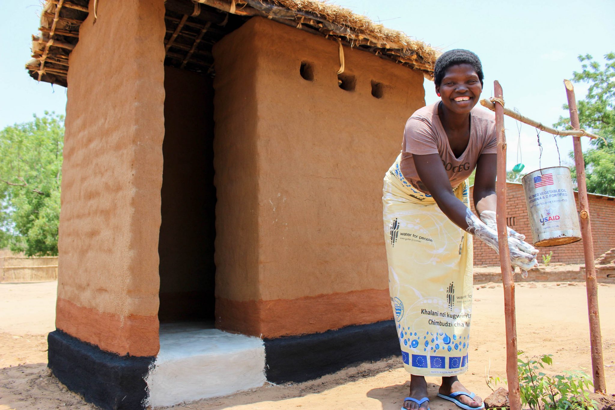 A woman smiles while washing her hands out front of a latrine structure