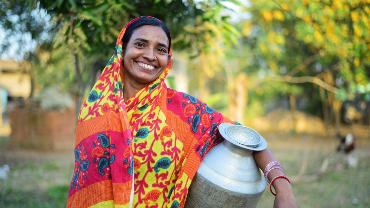 Photograph of a woman in a colorful sari holding a water container