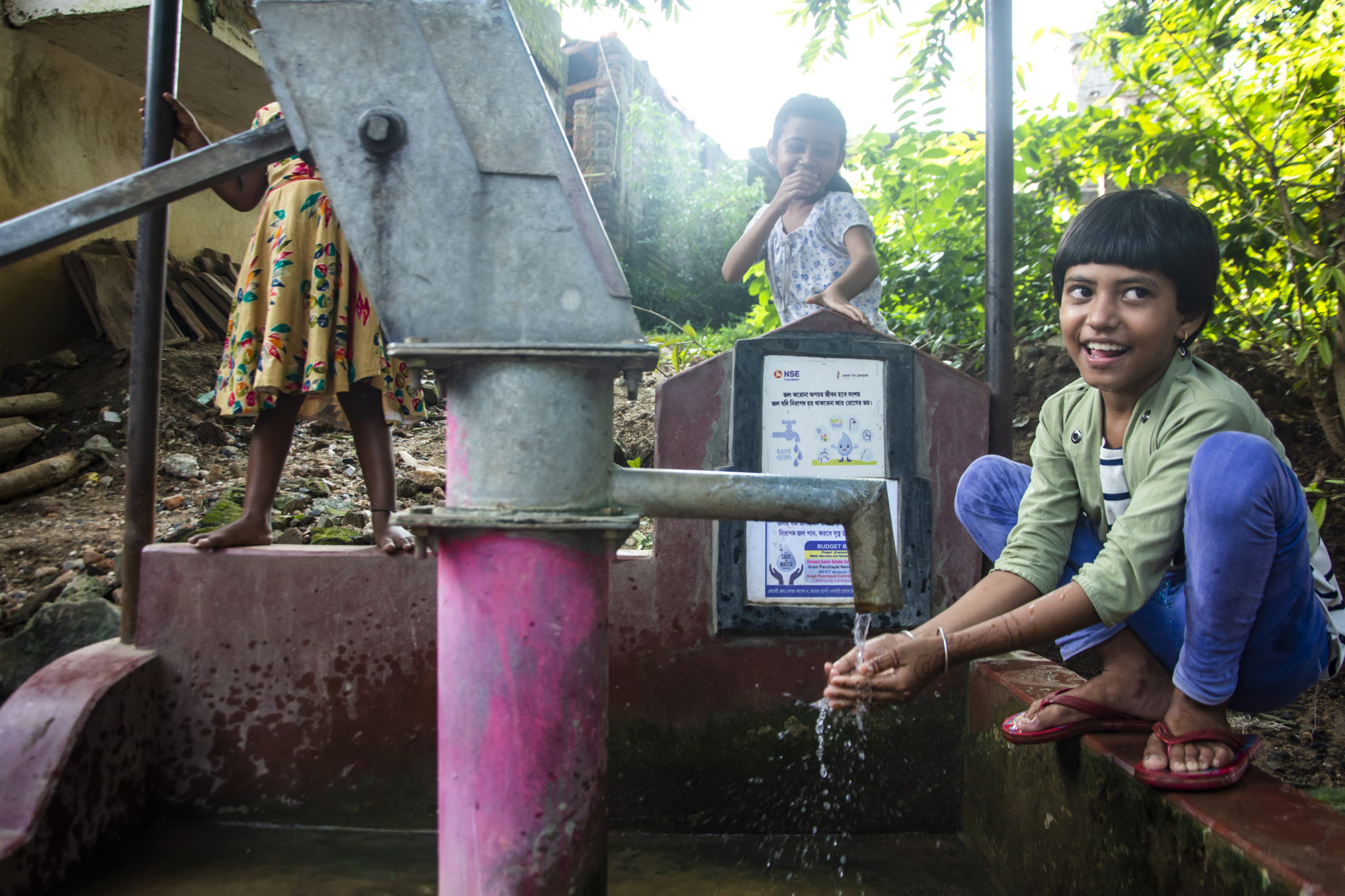 photograph of three children standing around a water pump