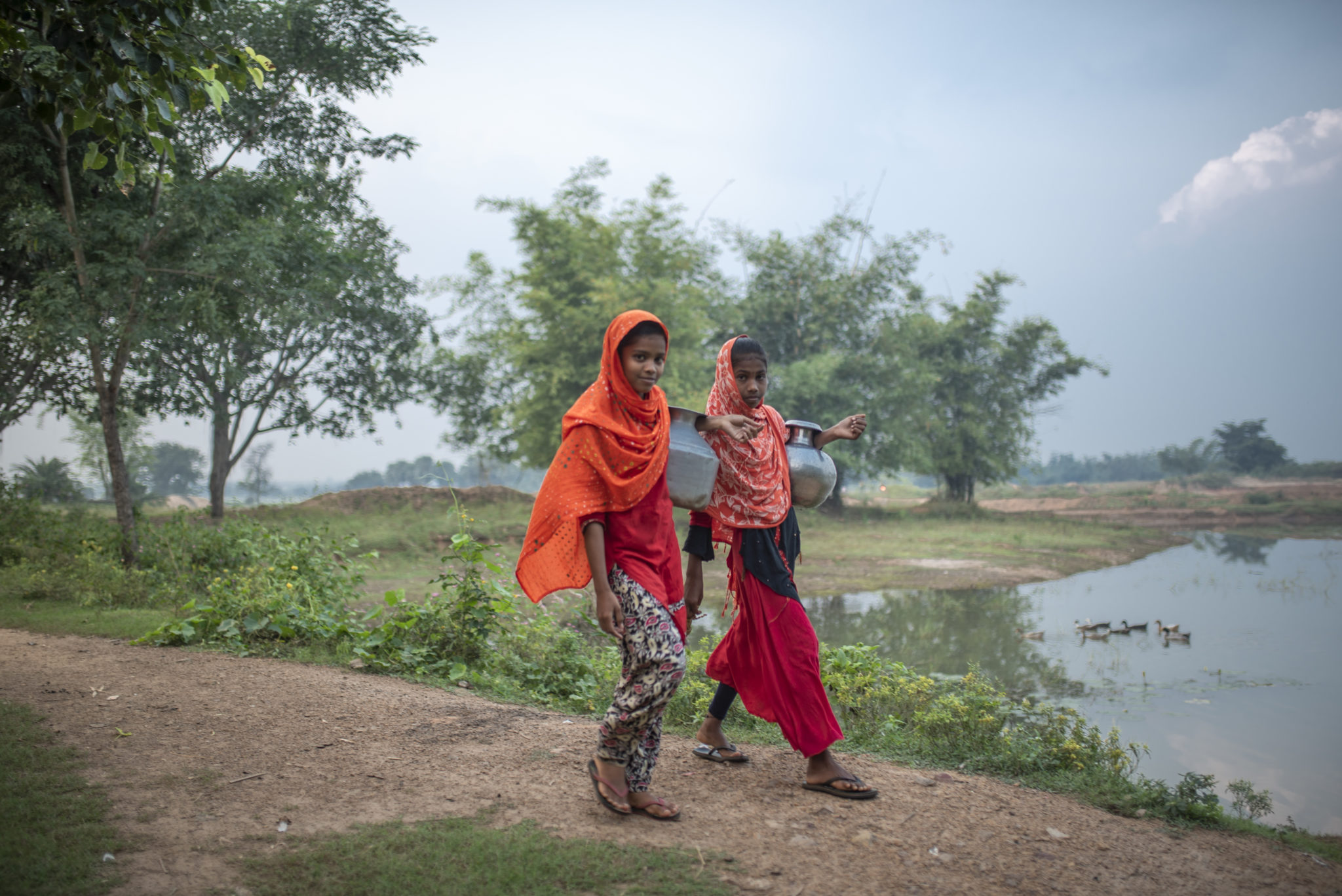 photograph of two young women walking with water containers in front of water