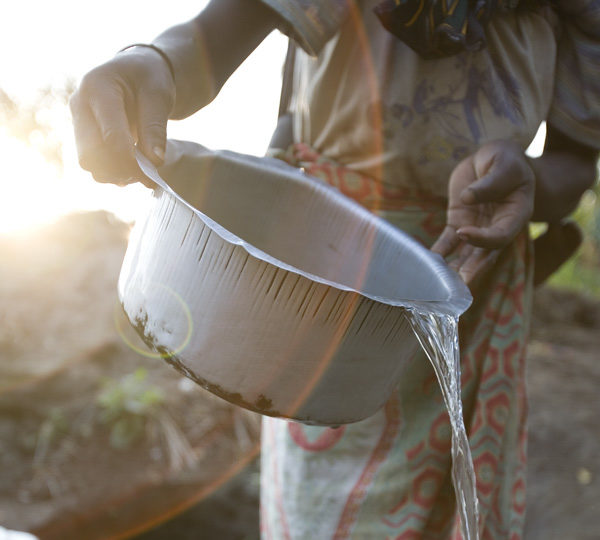 Photograph of a woman holding a tin pot of water