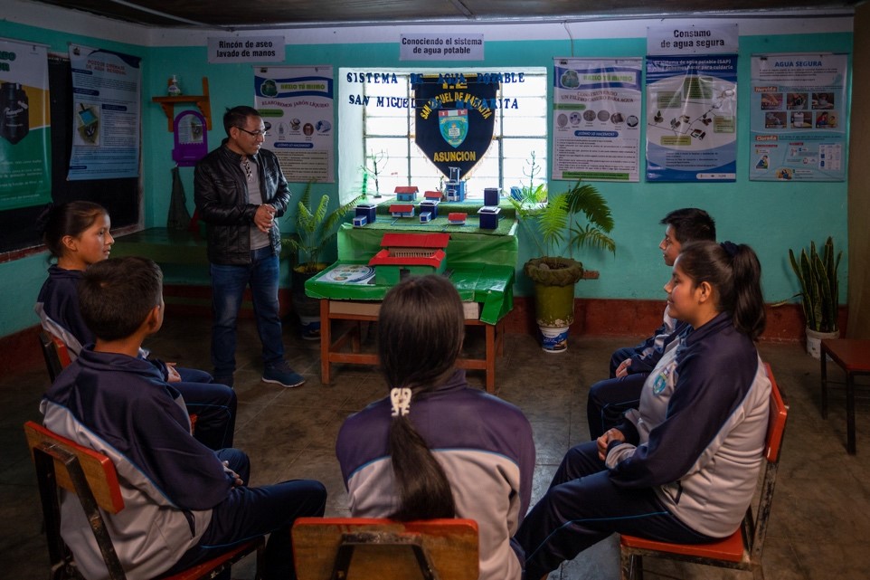 Photograph of a teacher in a classroom instructing students as they sit in a circle