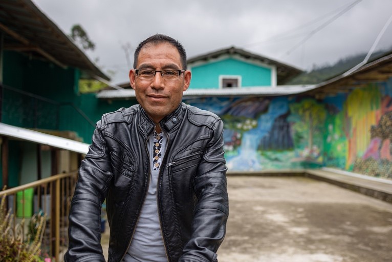 Photograph of a man smiling in front of a colorful mural