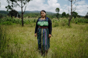 A woman, Teresa, in a green embroidered dress standing in front of trees.