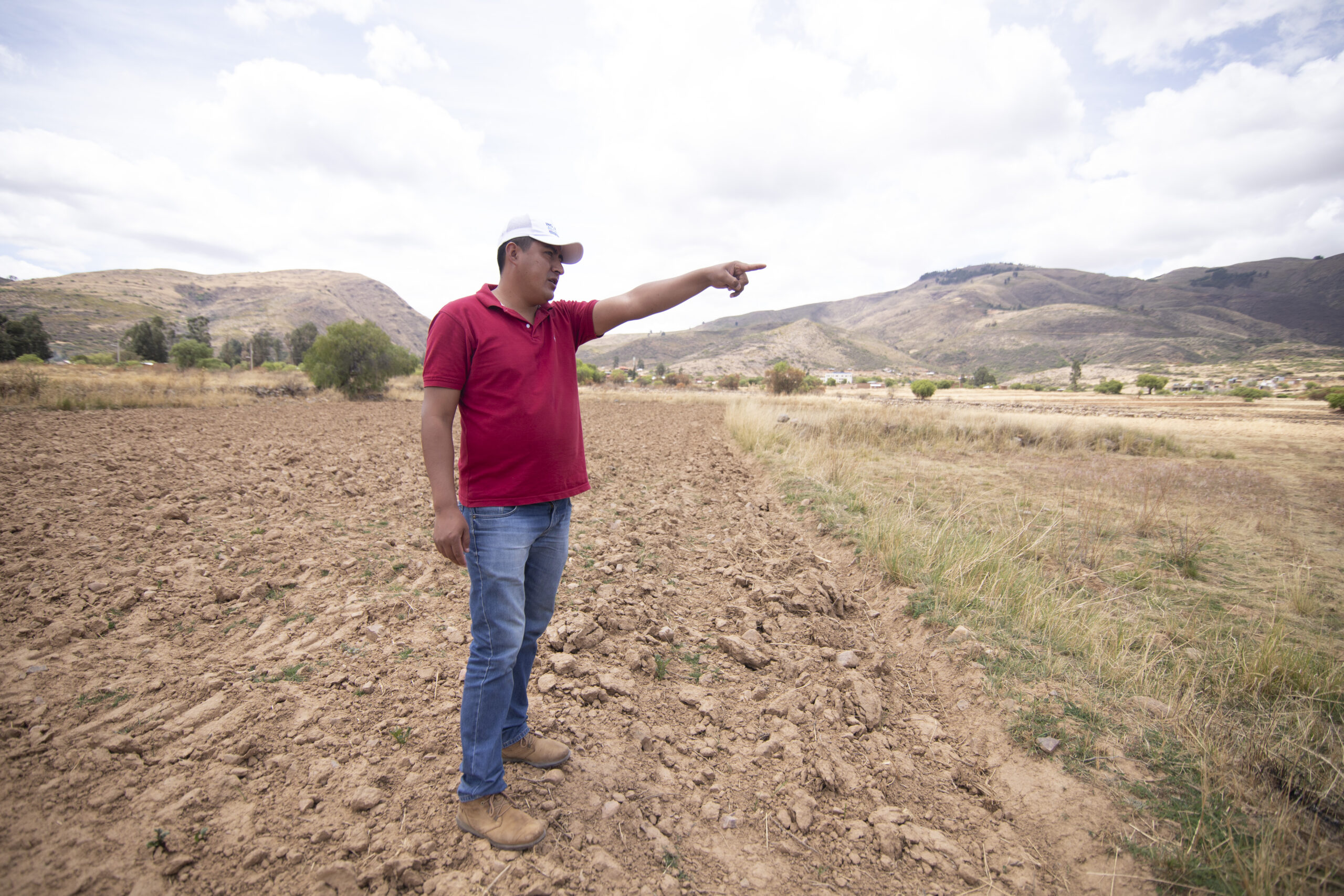 A man in a field with a dry ground points toward the right in the distance