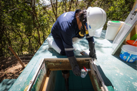 Wearing gloves and a hard hat, she checks and treats water inside a reservoir tank to ensure it is safe for the community.