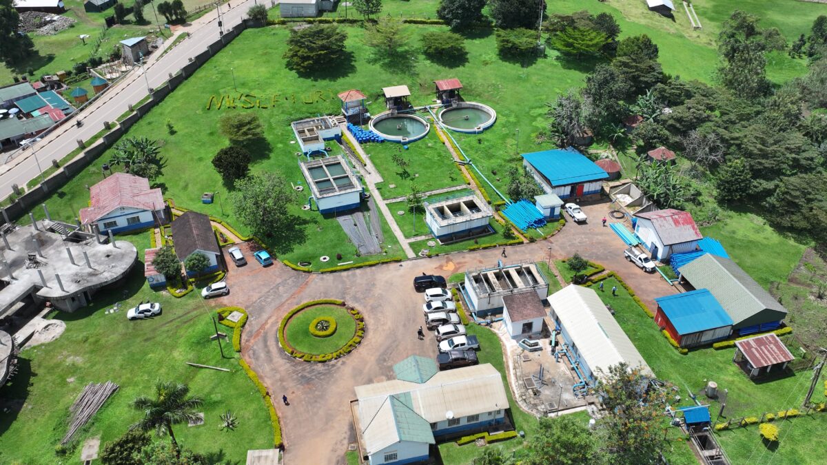 Aerial view of a water treatment plant facility with circular tanks, small buildings, access roads, and surrounding green grounds in Fort Portal