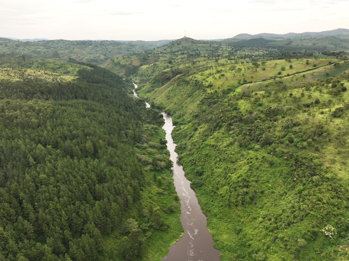 Aerial view of a narrow river cutting through rolling green hills and forested slopes