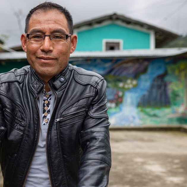 Photograph of a man smiling and standing in front of a colorful mural