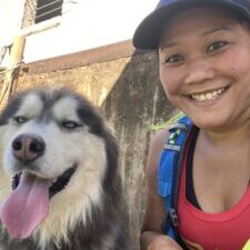 A woman in a baseball cap and red shirt with her dog, left, a husky.