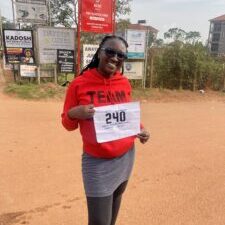 A woman in red holds a race bib with her number on it.