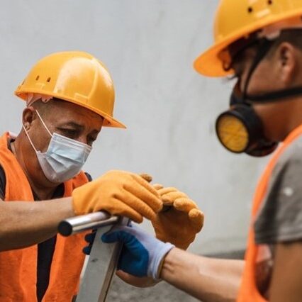 Photograph of two men in safety equipment hand pumping a septic tank